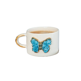 Handcrafted ceramic mug with a 3D blue butterfly design and a gold-plated handle, shown with coffee inside.