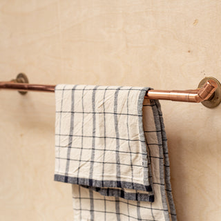 Copper towel rack with a plaid towel on a beige wall